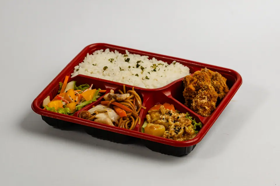 A bento box with rice, vegetables and fried chicken on white