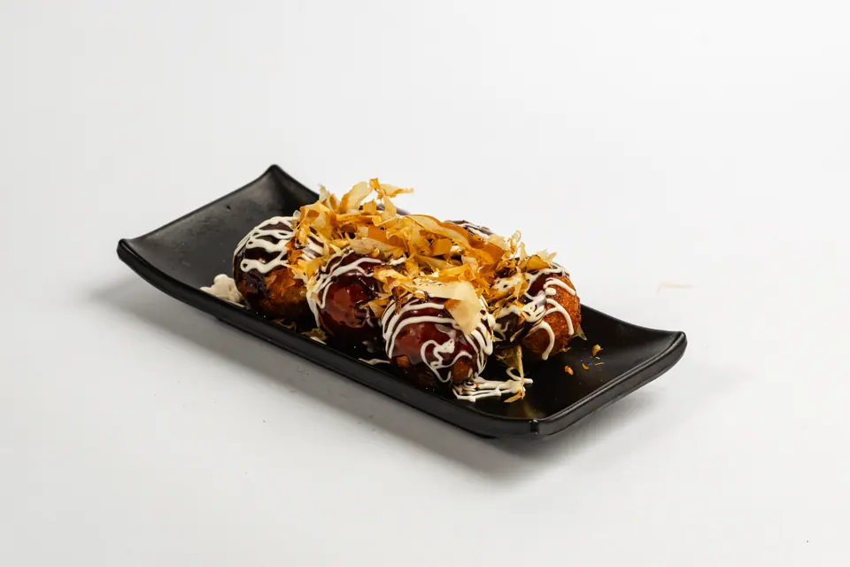 Takoyaki with mayonnaise and bonito flakes on a black plate