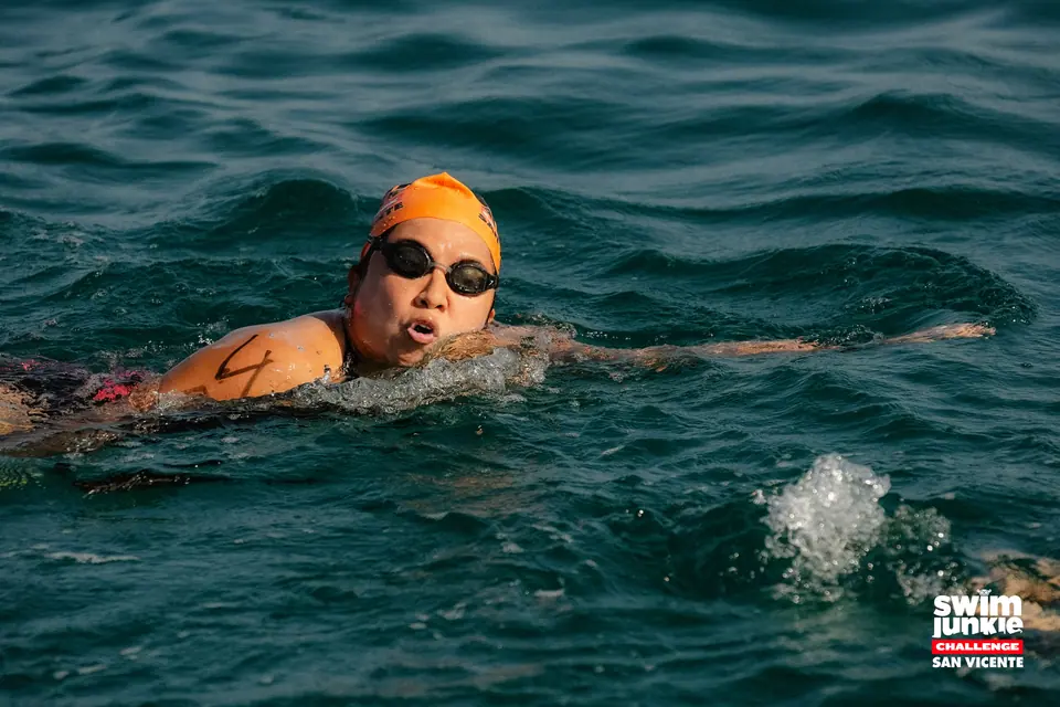A swimmer in an orange cap breathes mid-stroke in open water
