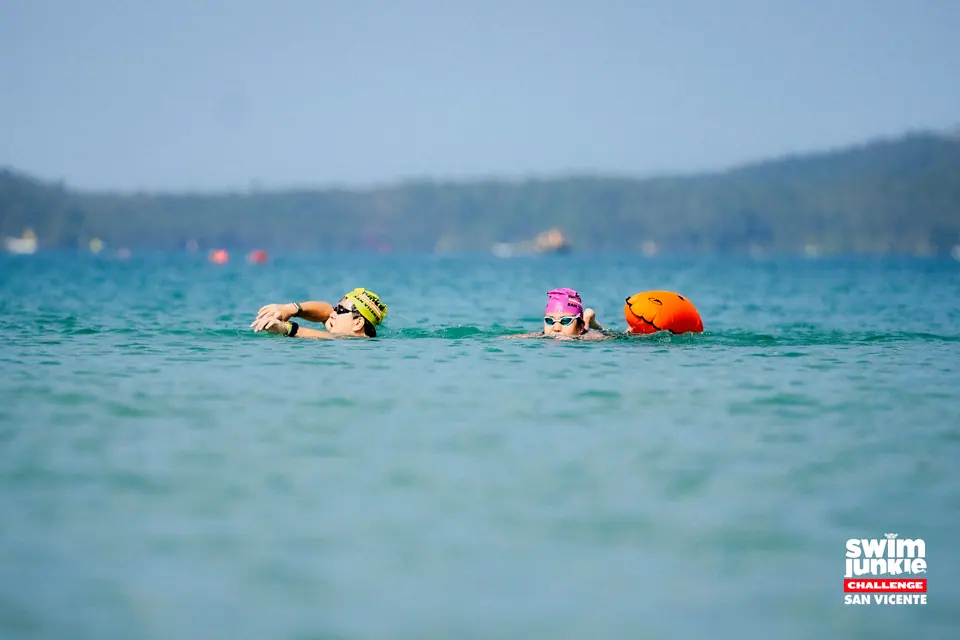 Swimmers with tow buoys cross a turquoise bay