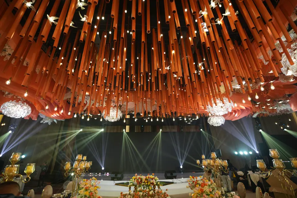 A ceiling of hanging orange fins and chandeliers over the ballroom