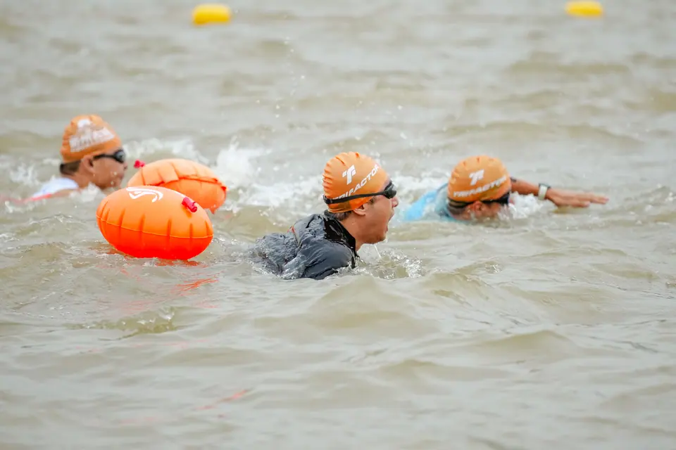 Swimmers with orange tow buoys in open water at the start of the swim leg