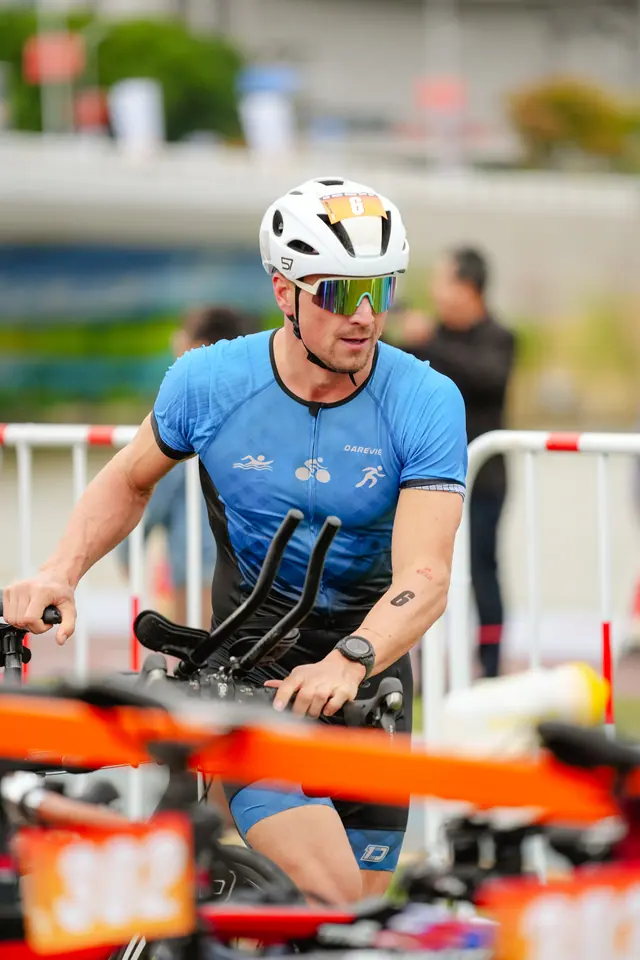 A triathlete in a blue suit runs his bike out of transition
