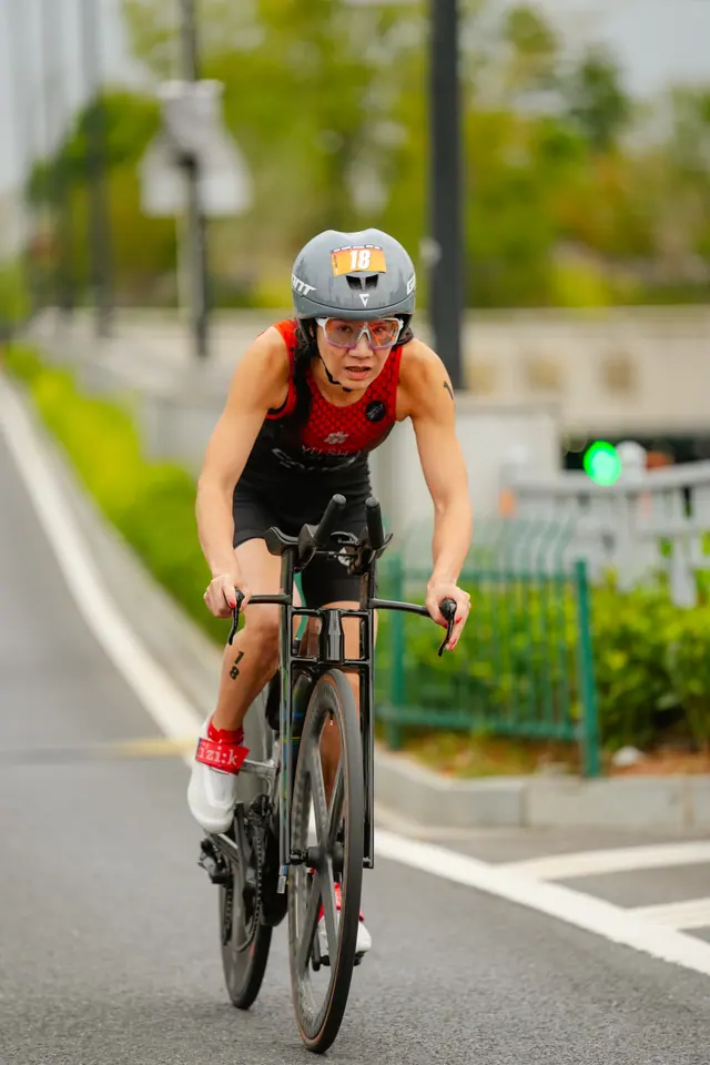 A cyclist in a red suit and silver helmet rides along a tree-lined path