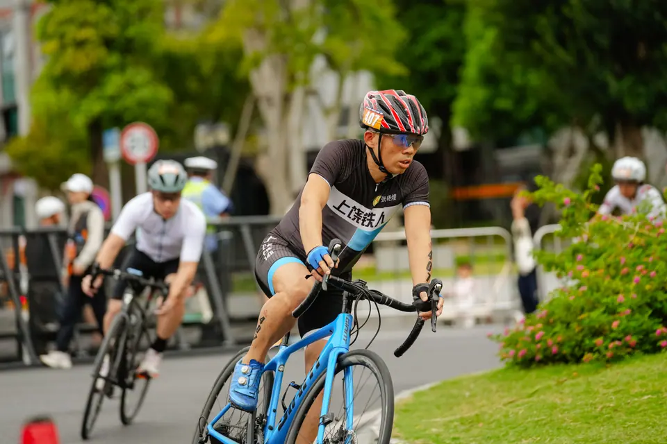A cyclist in a patterned helmet leads riders past the course barriers